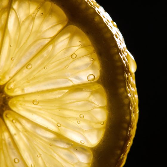 A backlit slice of lemon, glistening with juice against a dark background.